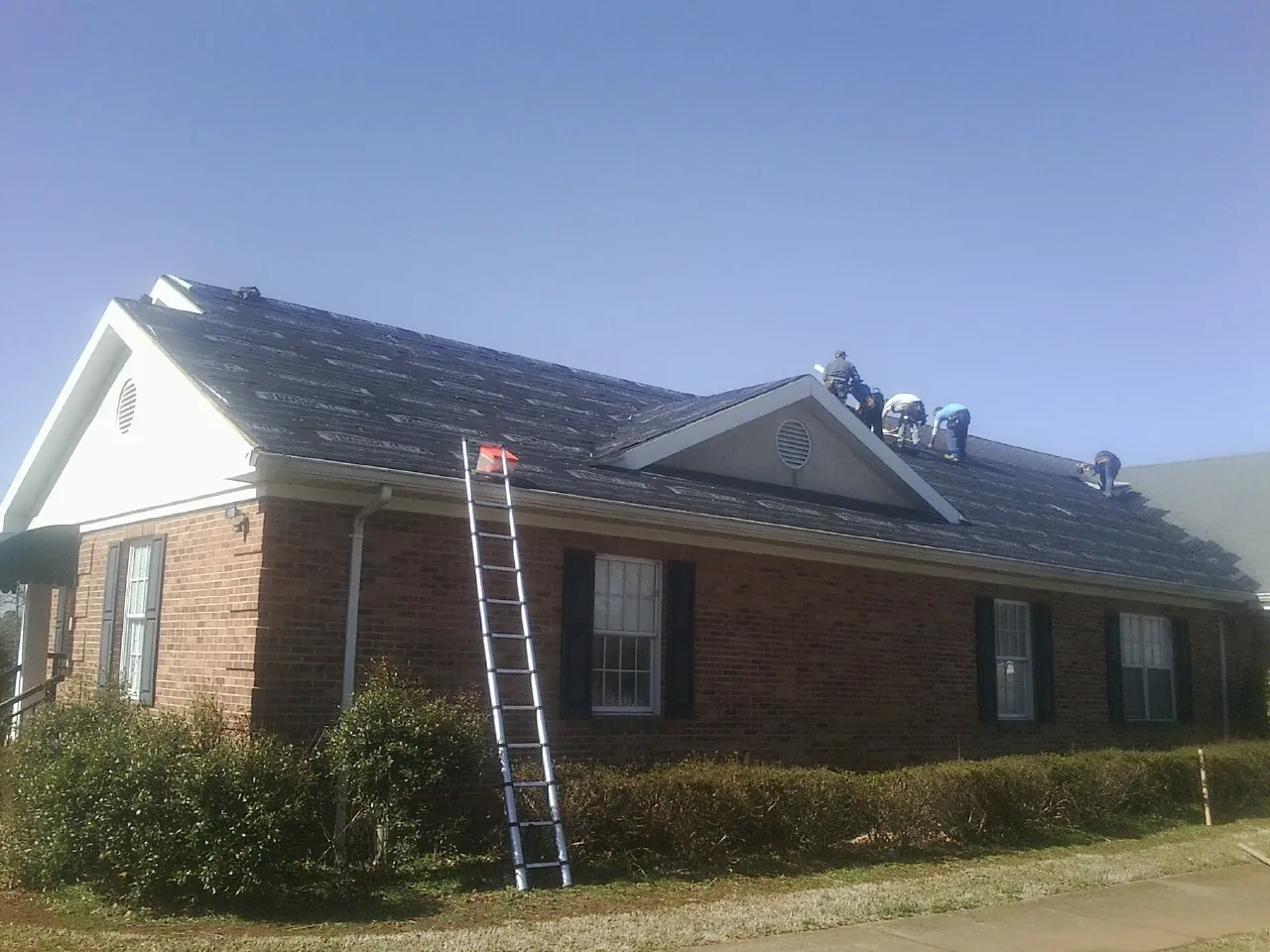 Crew tearing shingles off a brick ranch roof with a ladder set — Emergency Roof Repair work by our crew in Raeford