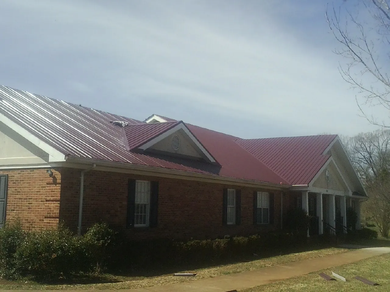 Red metal roof with gabled entries on a long brick building, from a Hail Damage Roof Repair job in Raeford