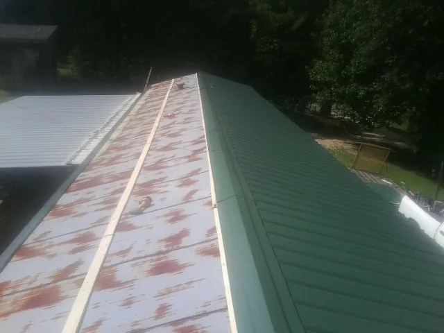 Old rusted panels beside newly installed green metal roofing — Wind Damage Roof Repair by Roofing Brothers in Raeford