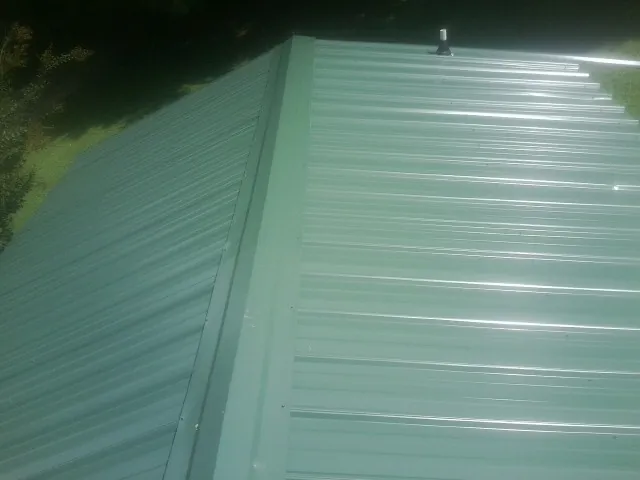 New green metal panels meeting at the ridge of a roof — Flat Roof Repair work by our crew in Raeford