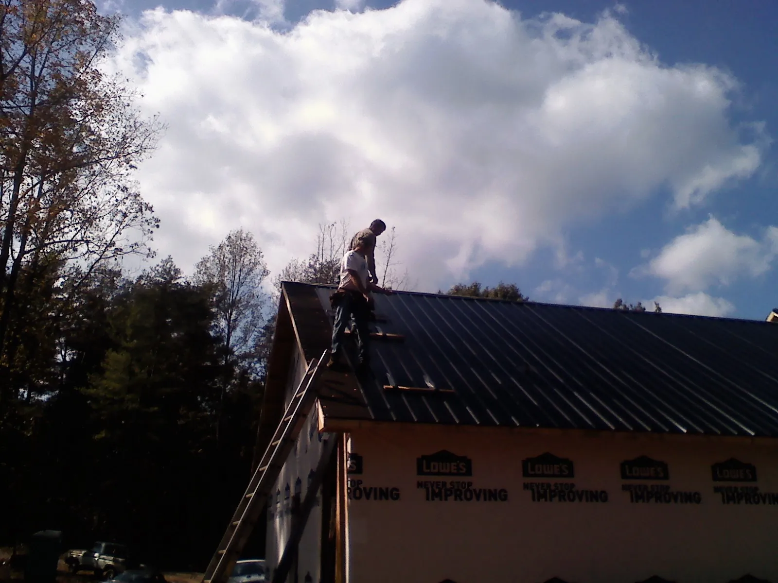 Roofer fastening dark metal panels high against a cloudy sky, from a Roof Inspection job in Raeford