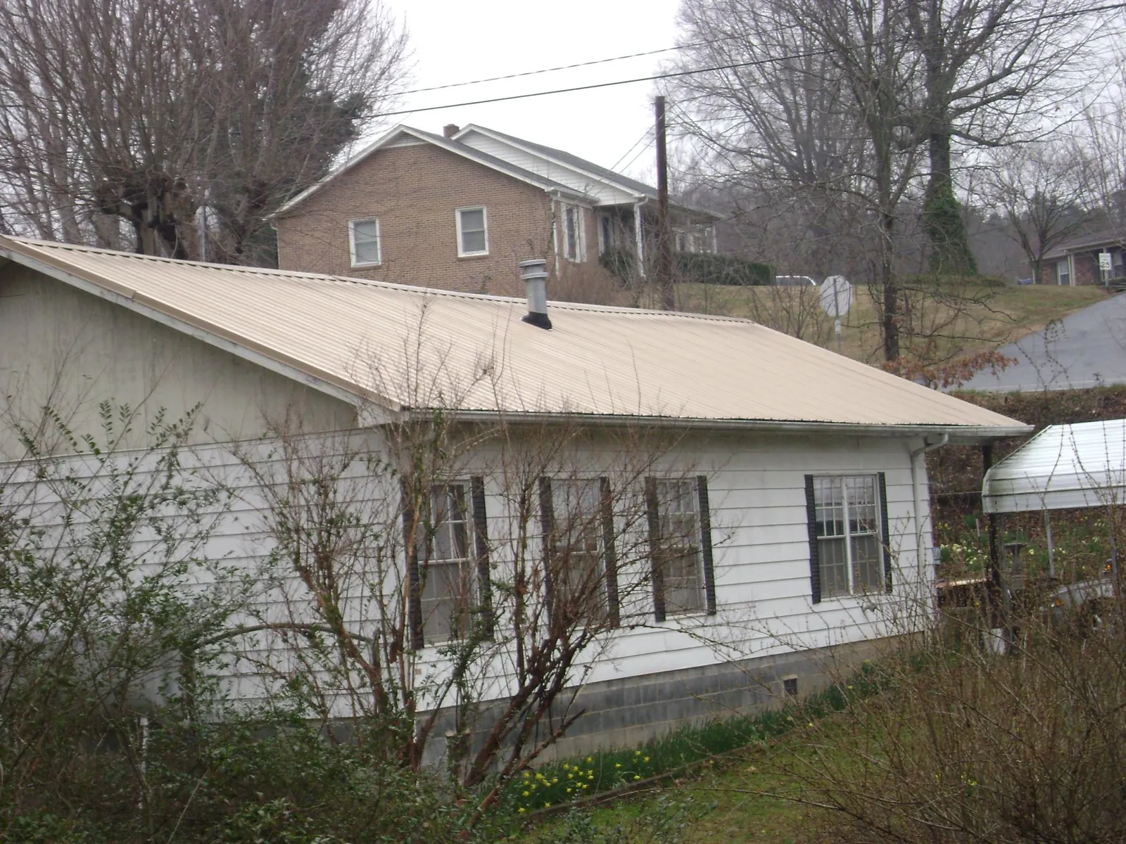 Tan metal roof on a white sided house set into a hillside — Commercial Roofing by Roofing Brothers in Raeford