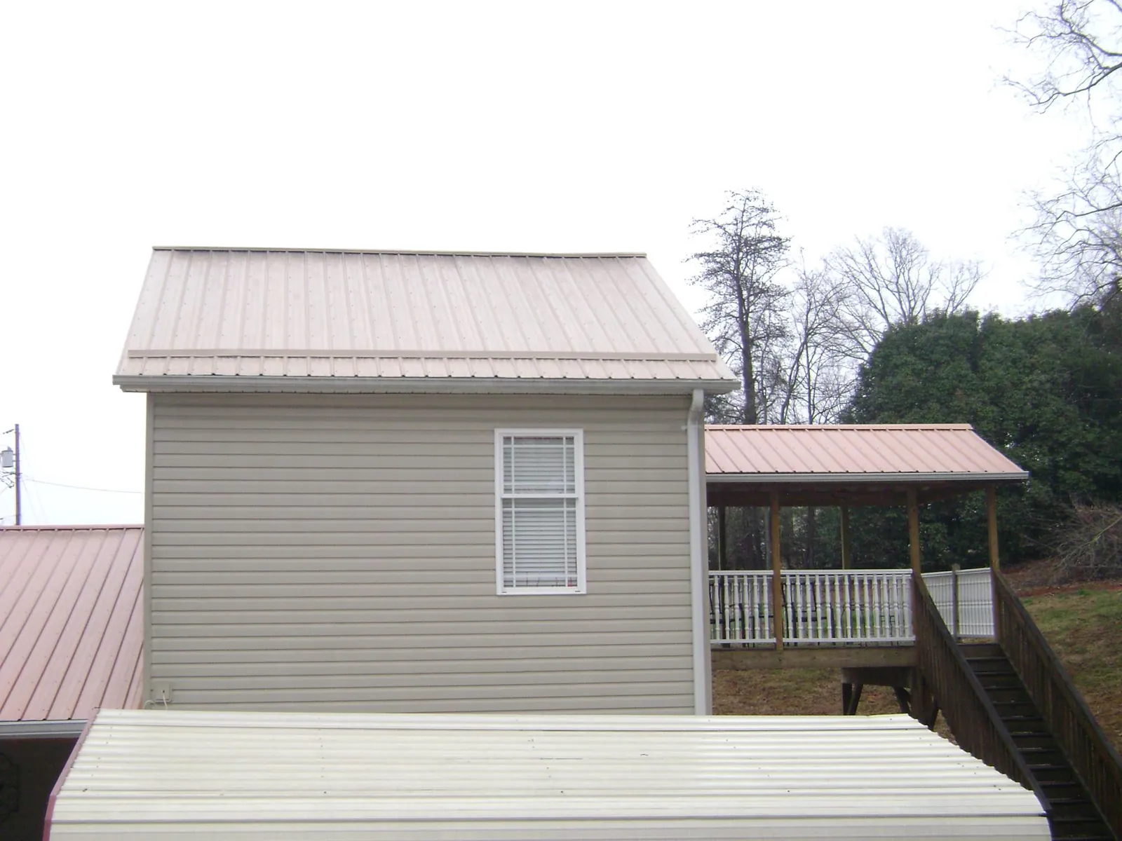 Tan metal roofs on a two story addition and attached porch, from a Roof Replacement job in Raeford